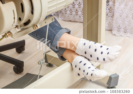 Female feet on the pedal of a sewing machine, motor 108383260