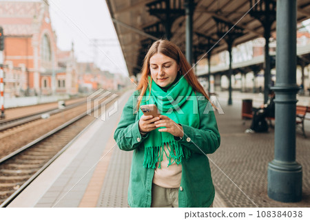A young and beautiful woman with backpack waiting for a train while using a mobile phone. Passenger using cellphone monitoring traffic schedule via application 108384038