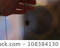 A woman's hand holds a pendulum in the form of a acorn on a dark background. 108384130