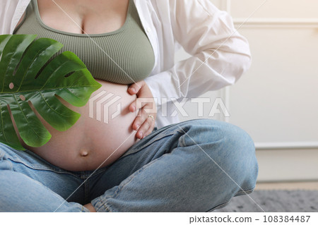 Close-up of torso of young pregnant model applying moisturizer on her belly to avoid stretch marks. Future mom. Pregnancy skincare concept 108384487