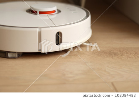 Wireless autonomous smart robotic vacuum cleaner is vacuuming floor with modern tiles at living room. Self-propelled cleaning robot. Floor cleaning system. Household remote control appliances. 108384488