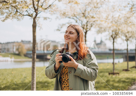 Happy Woman photographer with camera taking pictures outdoors. Home hobby, lifestyle, travel, people concept. 108385694