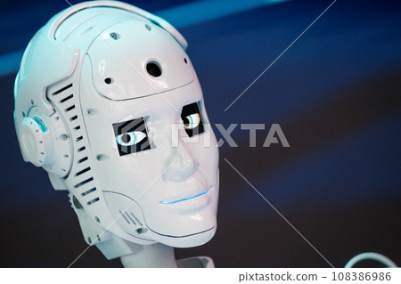 Closeup of white illuminated human robot looking to camera against blurred background 108386986