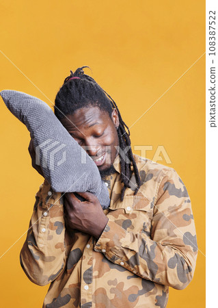 Dreamful person holding pillow to take a nap in studio, comfortable pose to sleep and rest. African american young adult with eyes closed trying to fix slpeeing schedule with bedtime hour. 108387522