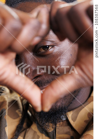 Excited man doing heart shape symbol in front of camera, smiling during valentine s day studio shot. African american person making love sign with fingers over yellow background. Positive concept Excited man doing heart shape symbol in front of camera, smiling during valentine s day studio shot. African american person making love sign with fingers over yellow background. Positive concept 108387568