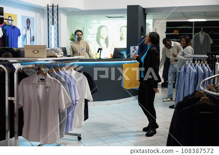 Satisfied customer holding shopping bags and smiling to cashier at clothing store checkout desk. Cheerful smiling asian woman carrying paper packages, standing in boutique 108387572