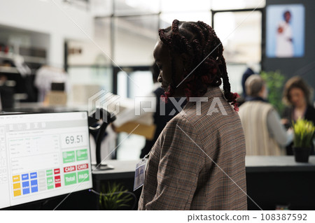 Showroom employee analyzing merchandise inventory on computer, working at clients purchase report in shopping centre. African american worker standing at cash register in modern boutique Showroom employee analyzing merchandise inventory on computer, working at clients purchase report in shopping centre. African american worker standing at cash register in modern boutique 108387592