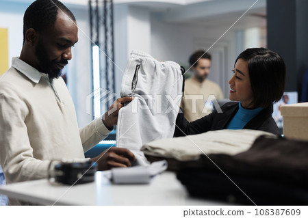 African american man getting assistance while selecting jogger pants in clothing store. Department mall boutique customer choosing casual apparel and talking with assistant 108387609