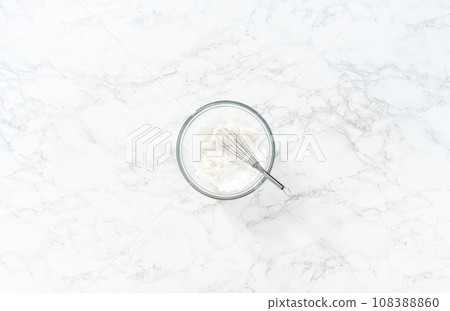 Mixing ingredients with a hand mixer in a large mixing bowl to make the lemon glaze for mini Easter bread kulich. 108388860