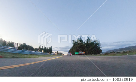 As the sun sets, driving on HWY 101 near Pismo Beach, California becomes a captivating experience with the sky painted in shades of orange and pink, casting a warm glow over the coastal landscape. 108388919