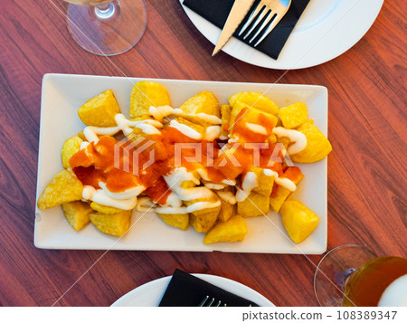 Spanish fried potatoes Patatas bravas served with cheese sauce 108389347