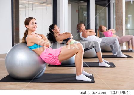 Sports people perform a back stretching exercise with a ball Sports people perform a back stretching exercise with a ball 108389641