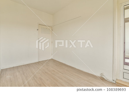 an empty room with white walls and wood flooring on one side, there is a door in the corner an empty room with white walls and wood flooring on one side, there is a door in the corner 108389693