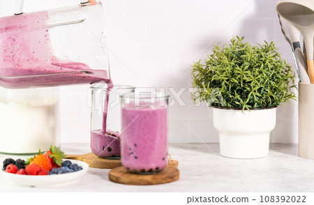 Pouring freshly made mixed berry boba smoothie into a drinking glass. 108392022
