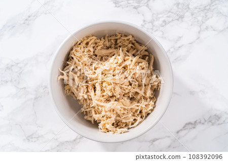 Shredded chicken in a pressure cooker. Freshly shredded chicken in a white bowl. 108392096
