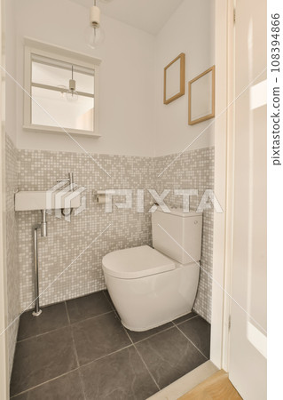 a white toilet in a small bathroom with grey tiles on the walls and floor to the right is a mirror a white toilet in a small bathroom with grey tiles on the walls and floor to the right is a mirror 108394866