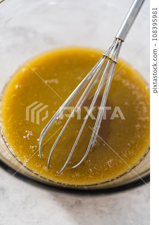 Mixing ingredients with a hand whisk to make sauce for bread pudding. 108395981