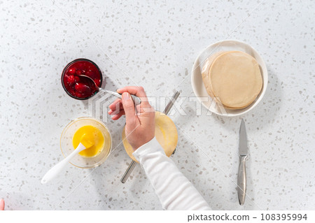 Flat lay. Filling empanada dough with cherry pie filling to make sweet cherry empanadas in the air fryer. Flat lay. Filling empanada dough with cherry pie filling to make sweet cherry empanadas in the air fryer. 108395994