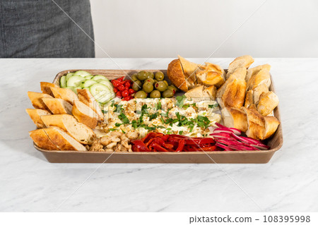 Arranging fresh and pickled vegetables on a serving tray to prepare a vegetarian party butter board for a party. Arranging fresh and pickled vegetables on a serving tray to prepare a vegetarian party butter board for a party. 108395998