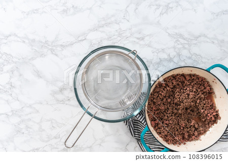 Flat lay. Draining brown ground beef meshed strainer to make homemade hamburger helper. 108396015