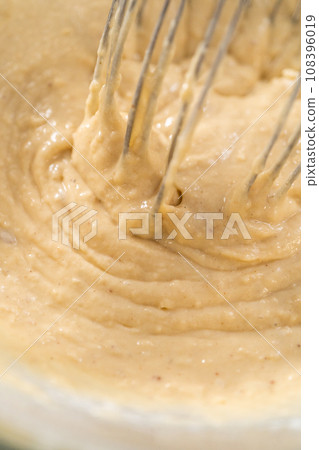Mixing wet and dry ingredients with a hand whisk in a glass mixing bowl to prepare eggnog pancakes. Mixing wet and dry ingredients with a hand whisk in a glass mixing bowl to prepare eggnog pancakes. 108396019