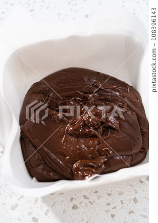 Filling square glass baking pan lined with parchment paper with fudge mixture to prepare caramel fudge. 108396143