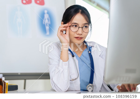 Medical Doctor in Glasses is Working on a Desktop Computer in a Health Clinic Medical Doctor in Glasses is Working on a Desktop Computer in a Health Clinic 108396159