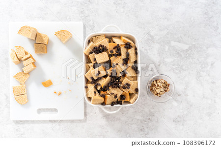 Flat lay. Baking bread pudding with raising and almond slivers in a white casserole dish. 108396172