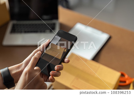 Selling online by taking photo of clothes with phone app and doing e-commerce business woman at home with shipping boxes 108396253