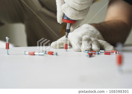A male worker tightens fasteners on parts of cabinet furniture. A male worker tightens fasteners on parts of cabinet furniture. 108398301