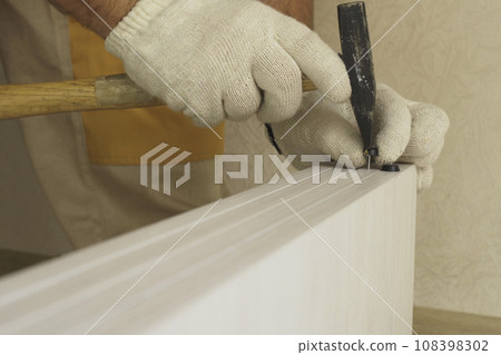 A worker hammers a furniture support - a nail - to a piece of cabinet furniture. A worker hammers a furniture support - a nail - to a piece of cabinet furniture. 108398302