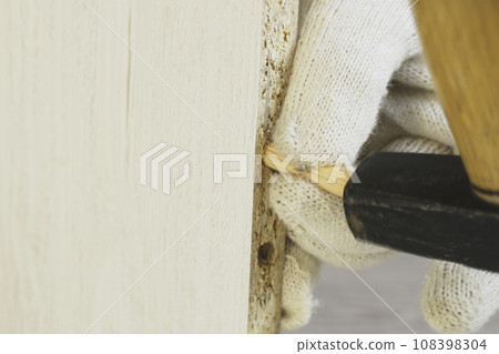 A worker hammers a wooden dowel into a hole in cabinet furniture. 108398304