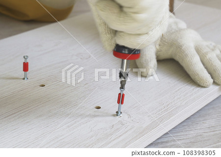 A male worker tightens fasteners on parts of cabinet furniture. A male worker tightens fasteners on parts of cabinet furniture. 108398305