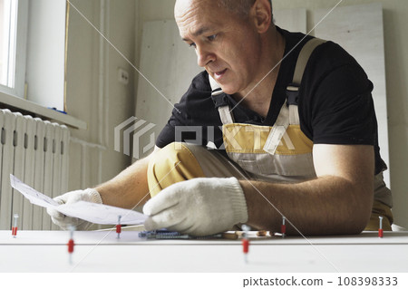 A male worker studies instructions before assembling furniture. A male worker studies instructions before assembling furniture. 108398333
