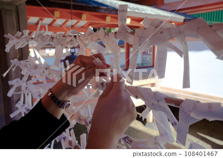 Hand of a woman tying fortunes drawn at Itsukushima Shrine in Hiroshima Prefecture 02 108401467