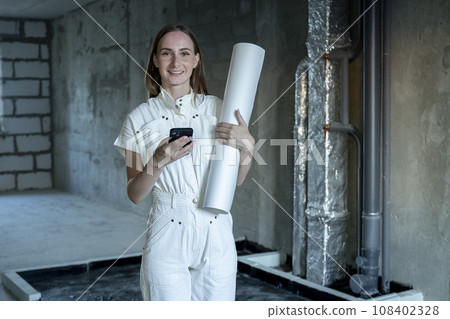 Young attractive female architect looks at the apartment plan on her smartphone during the renovation 108402328