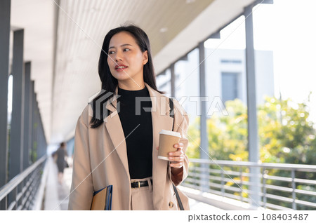 A beautiful Asian businesswoman is walking along a skywalk in the city with her takeaway coffee cup. 108403487