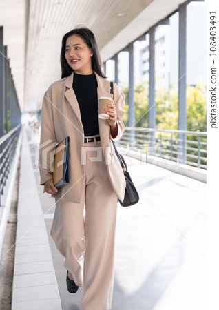 A confident Asian businesswoman is walking on the skywalk in the city with her stuff. A confident Asian businesswoman is walking on the skywalk in the city with her stuff. 108403491