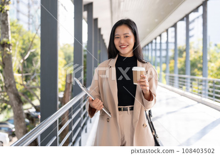 A beautiful Asian businesswoman is standing on the skywalk and smiling at the camera. A beautiful Asian businesswoman is standing on the skywalk and smiling at the camera. 108403502