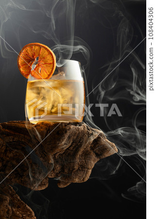 Smoked old fashioned cocktail with ice and dried orange slice. 108404306