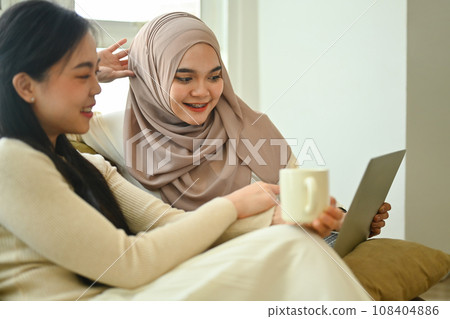 Happy young Muslim woman watching video or surfing internet laptop with her best friend Happy young Muslim woman watching video or surfing internet laptop with her best friend 108404886
