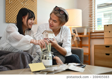 Young couple sitting in living room calculating expenses, managing finances and save money for future Young couple sitting in living room calculating expenses, managing finances and save money for future 108405083