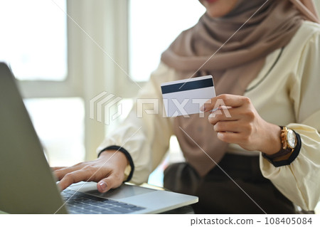 Muslim woman holding credit card using laptop doing online banking transaction or shopping in online store. Muslim woman holding credit card using laptop doing online banking transaction or shopping in online store. 108405084