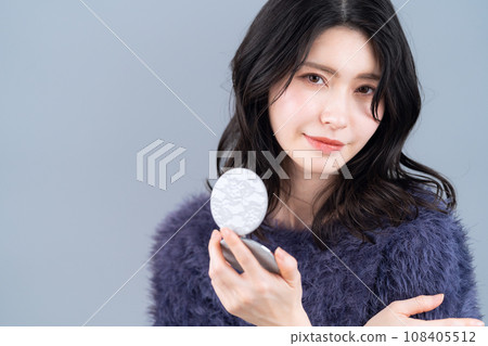 A middle-aged woman doing skin care against a gray background 108405512