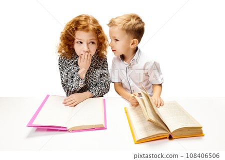 Cute redhead, curly girl sitting at desk with little boy who quietly tells her secret. Child study and learn for preschool. Online education. Cute redhead, curly girl sitting at desk with little boy who quietly tells her secret. Child study and learn for preschool. Online education. 108406506