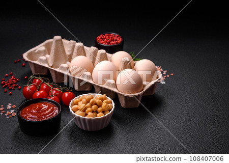Raw chicken eggs in a box, cherry tomatoes, chickpeas, spices, salt and herbs Raw chicken eggs in a box, cherry tomatoes, chickpeas, spices, salt and herbs 108407006
