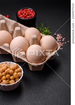 Raw chicken eggs in a box, cherry tomatoes, chickpeas, spices, salt and herbs 108407010
