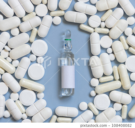 Mix of white medical capsules and pills with ampoule in the middle on light blue top view 108408082