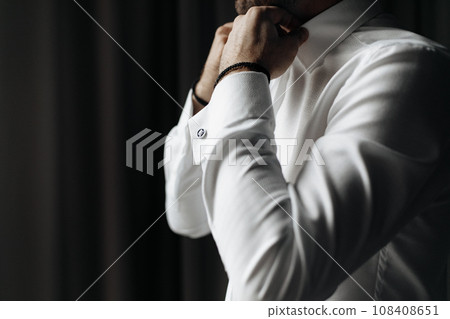 Close up cropped picture of caucasian male adjusting collar of a white shirt. Groom preparing for wedding. 108408651