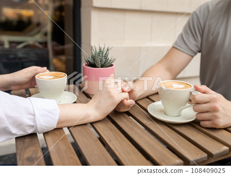 Traditional couple holding hands and coffee cups on a wooden table. 108409025